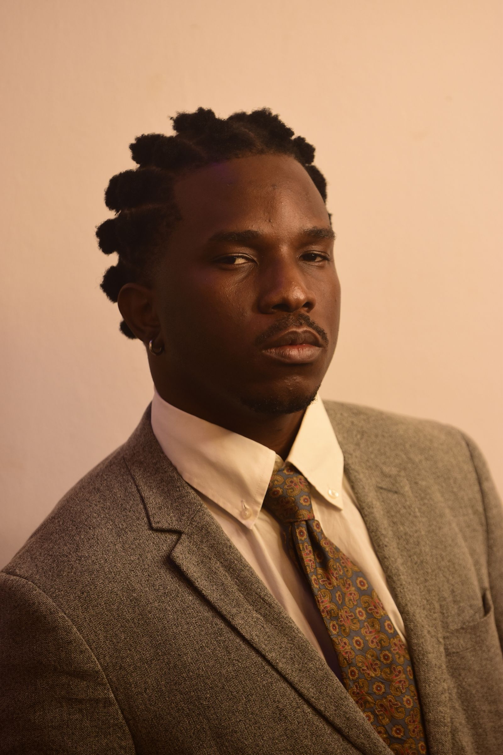 A businessman in a tweed jacket and tie looks calmly to the camera in a warm studio portrait.