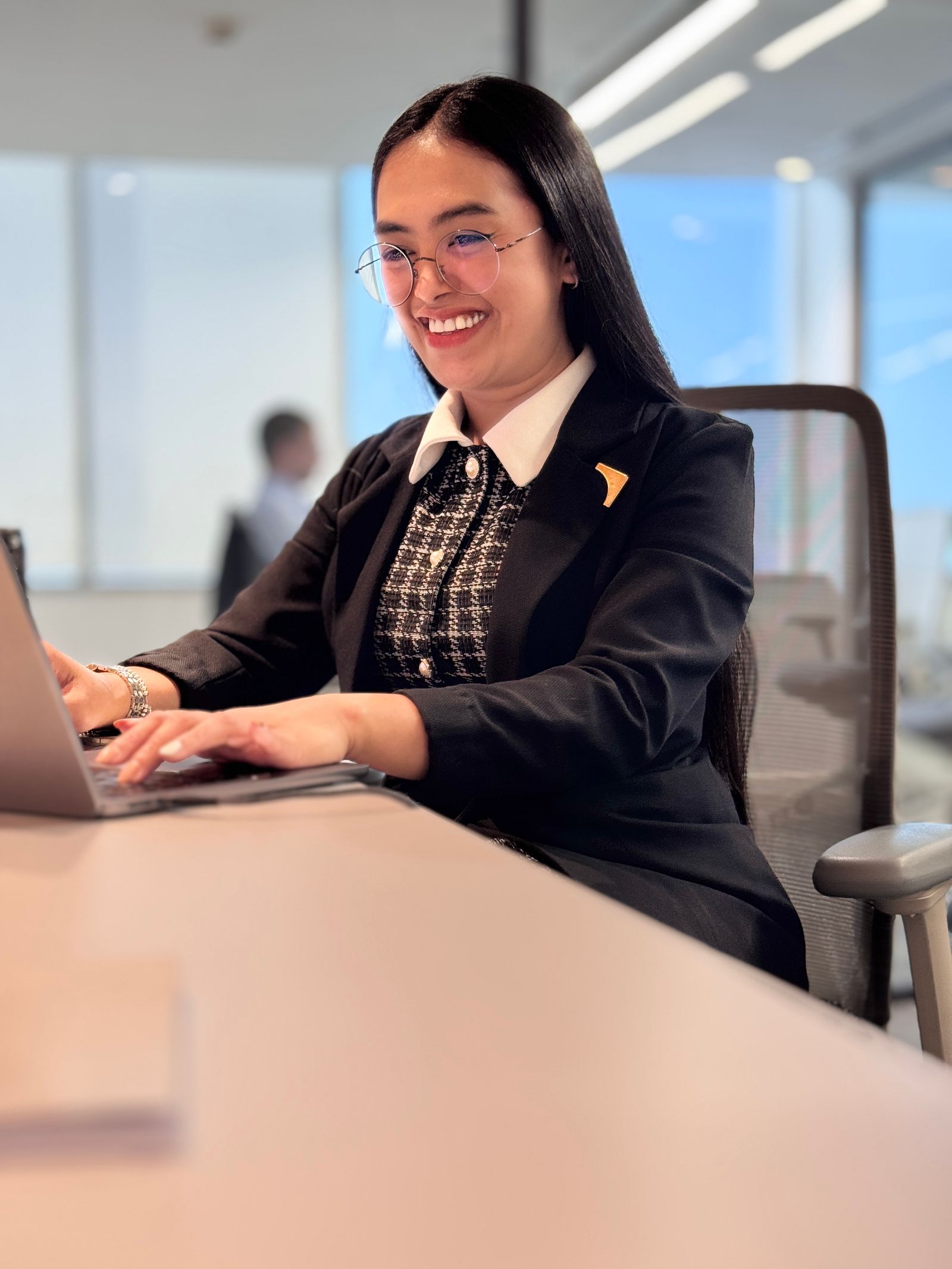 An executive smiles at the screen of her laptop from her seat in a corporate meeting room.